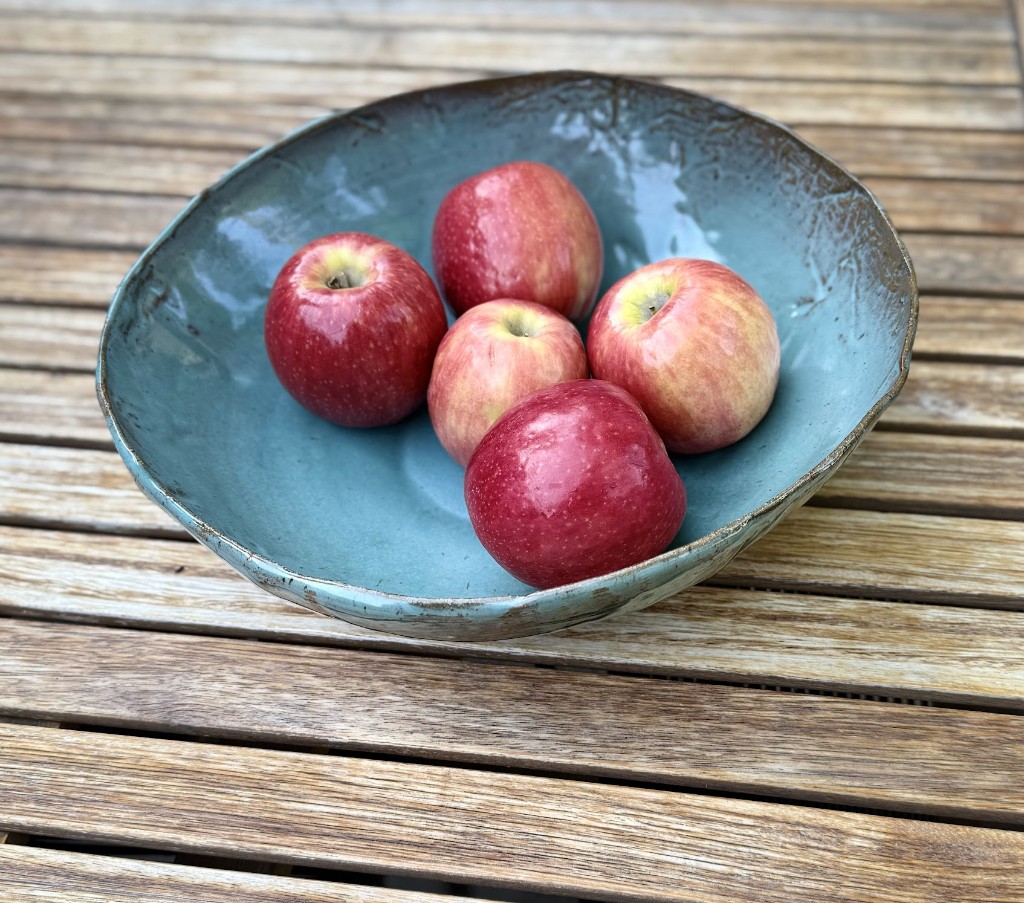 Handcrafted teal bowl with apples on a wooden table
